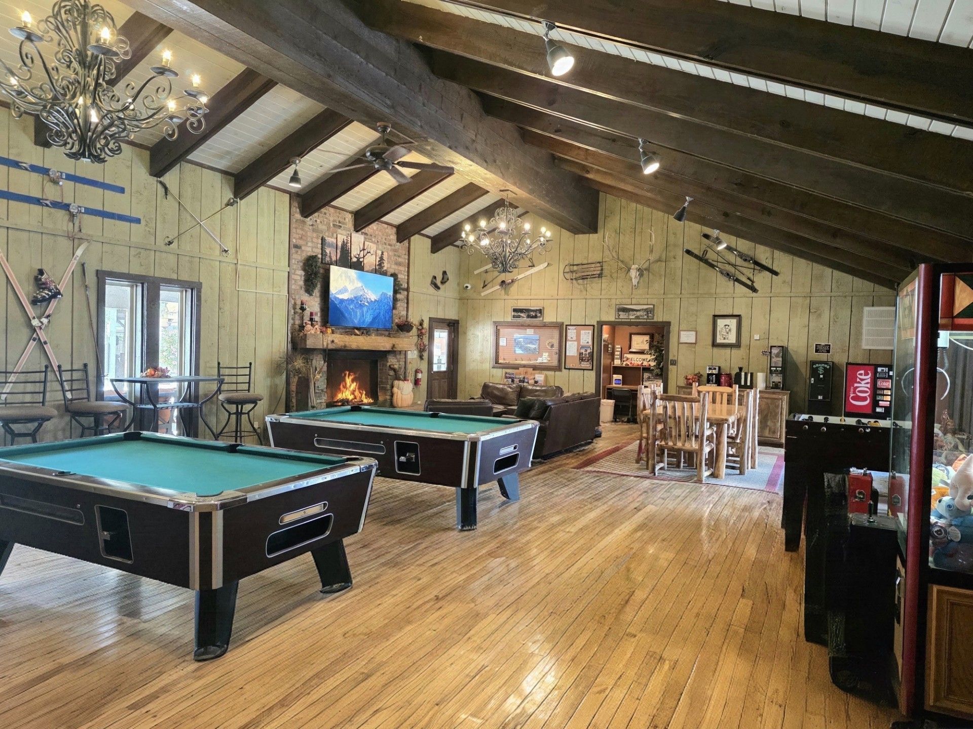Rustic game room with pool tables, wood floors, TV, and bar seating under a sloped ceiling