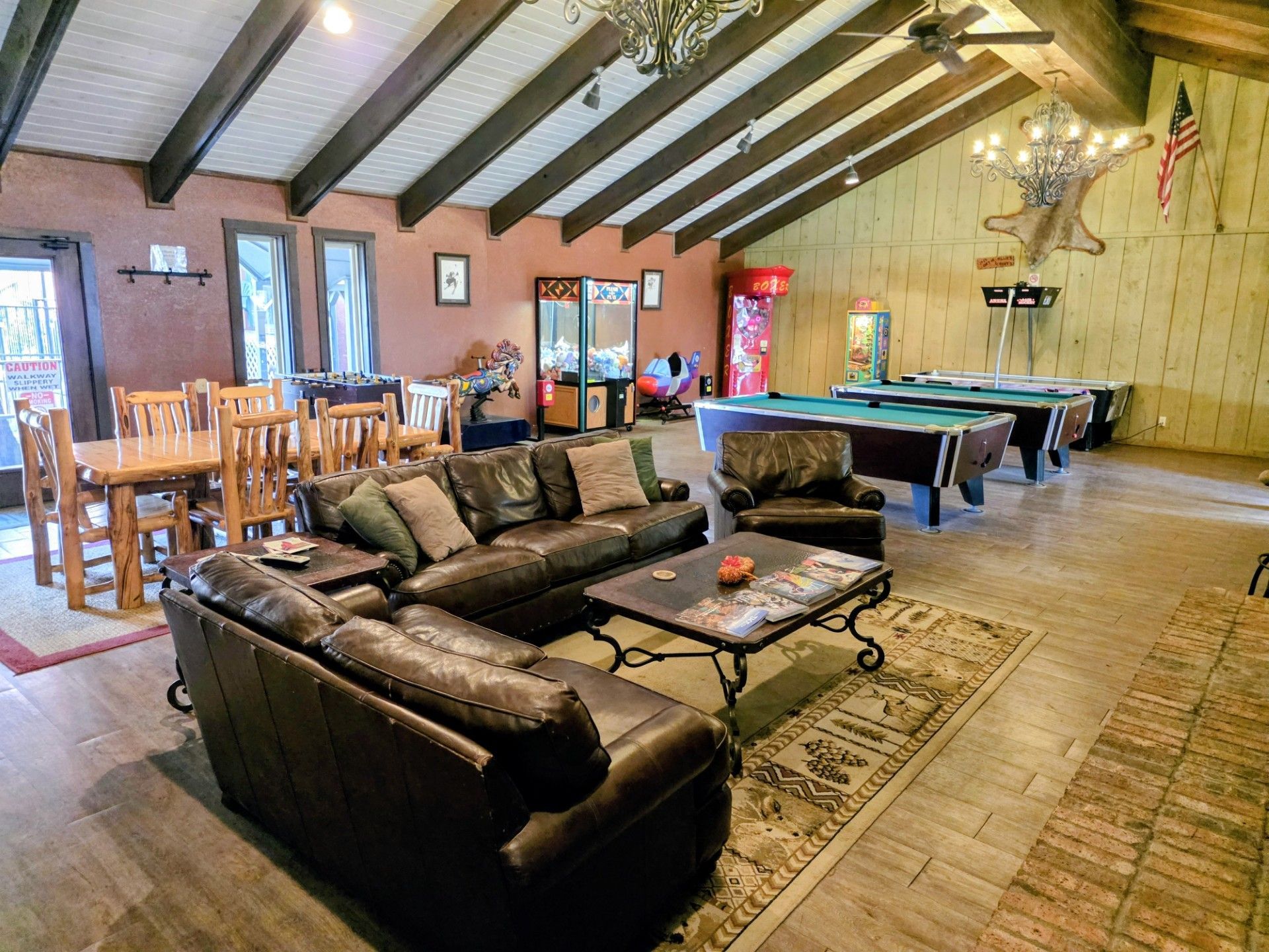 Rustic lounge with leather sofas, pool tables, wooden beams, and a patterned rug in a cabin-style rec room