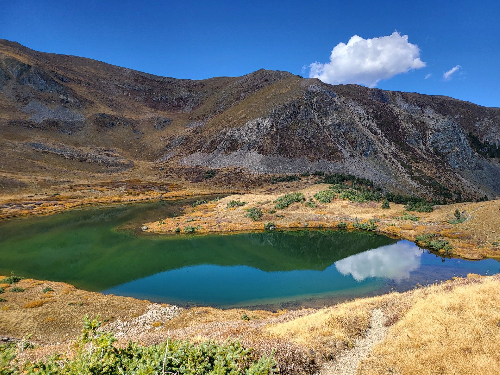 Mountain lake with green water, rocky slopes, and a blue sky with a single white cloud.