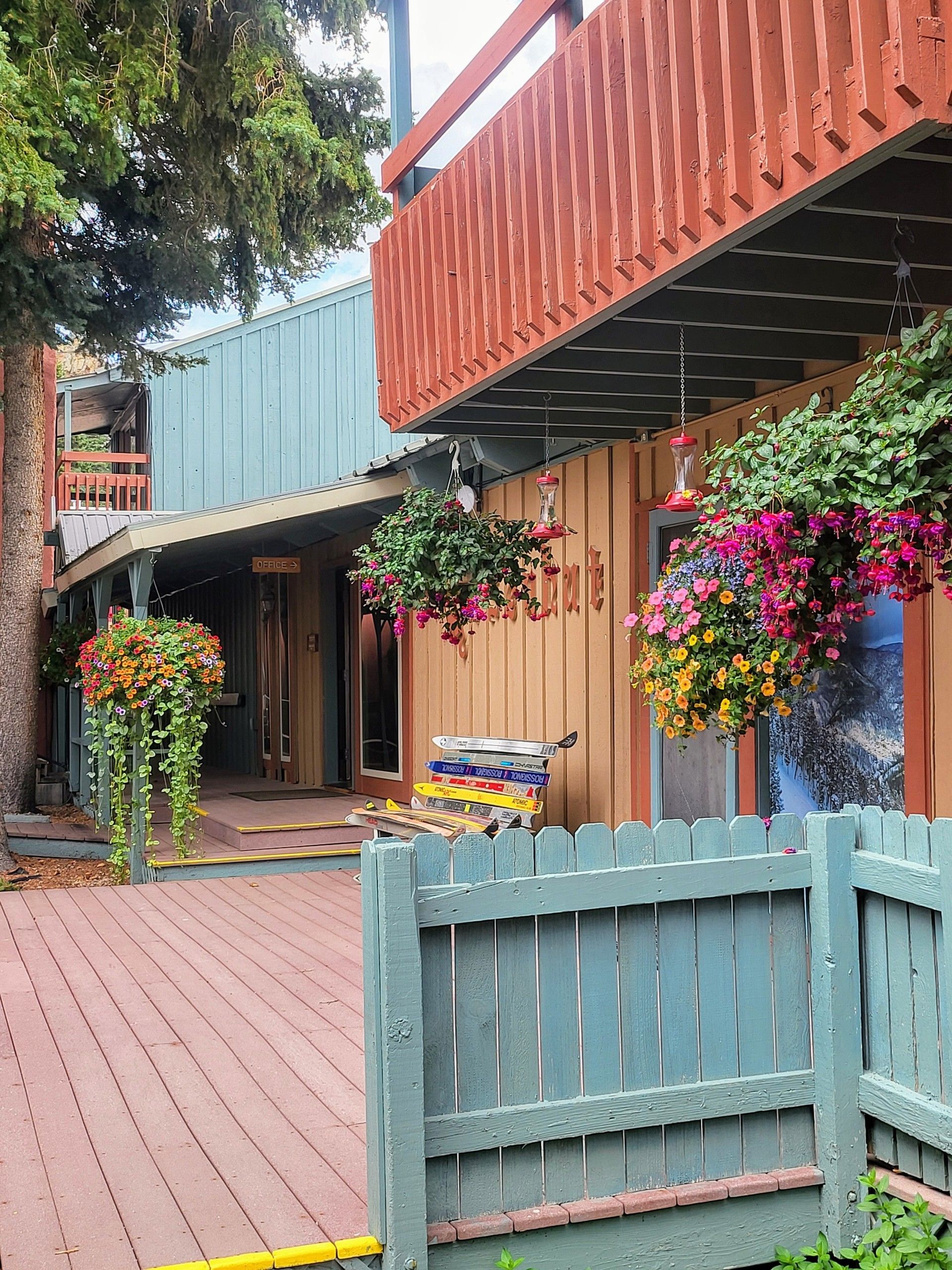 Colorful courtyard with hanging flowers, wooden deck, and pastel fences beside modern cabins