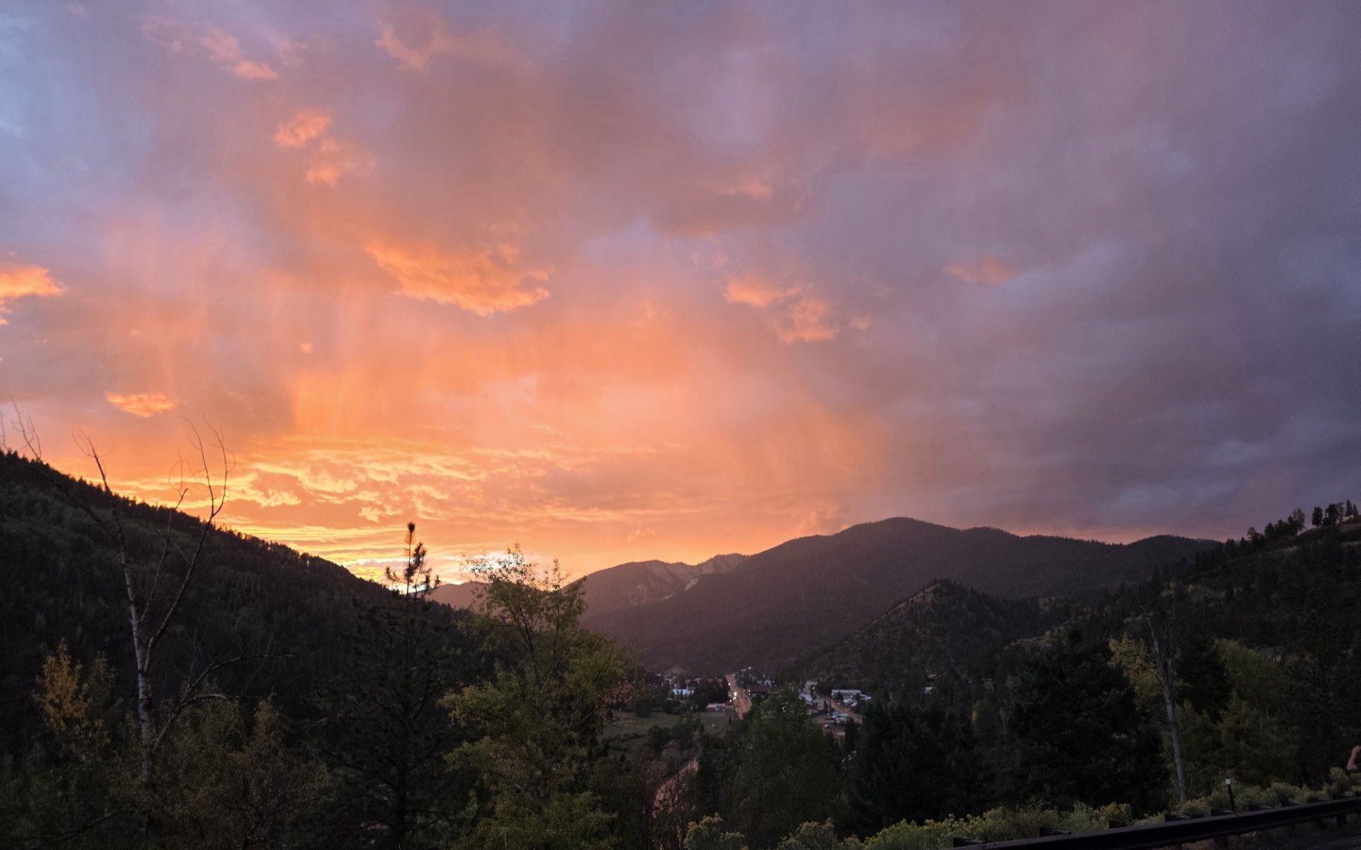 Sunset over dark mountains and trees, with orange-pink clouds glowing in the sky