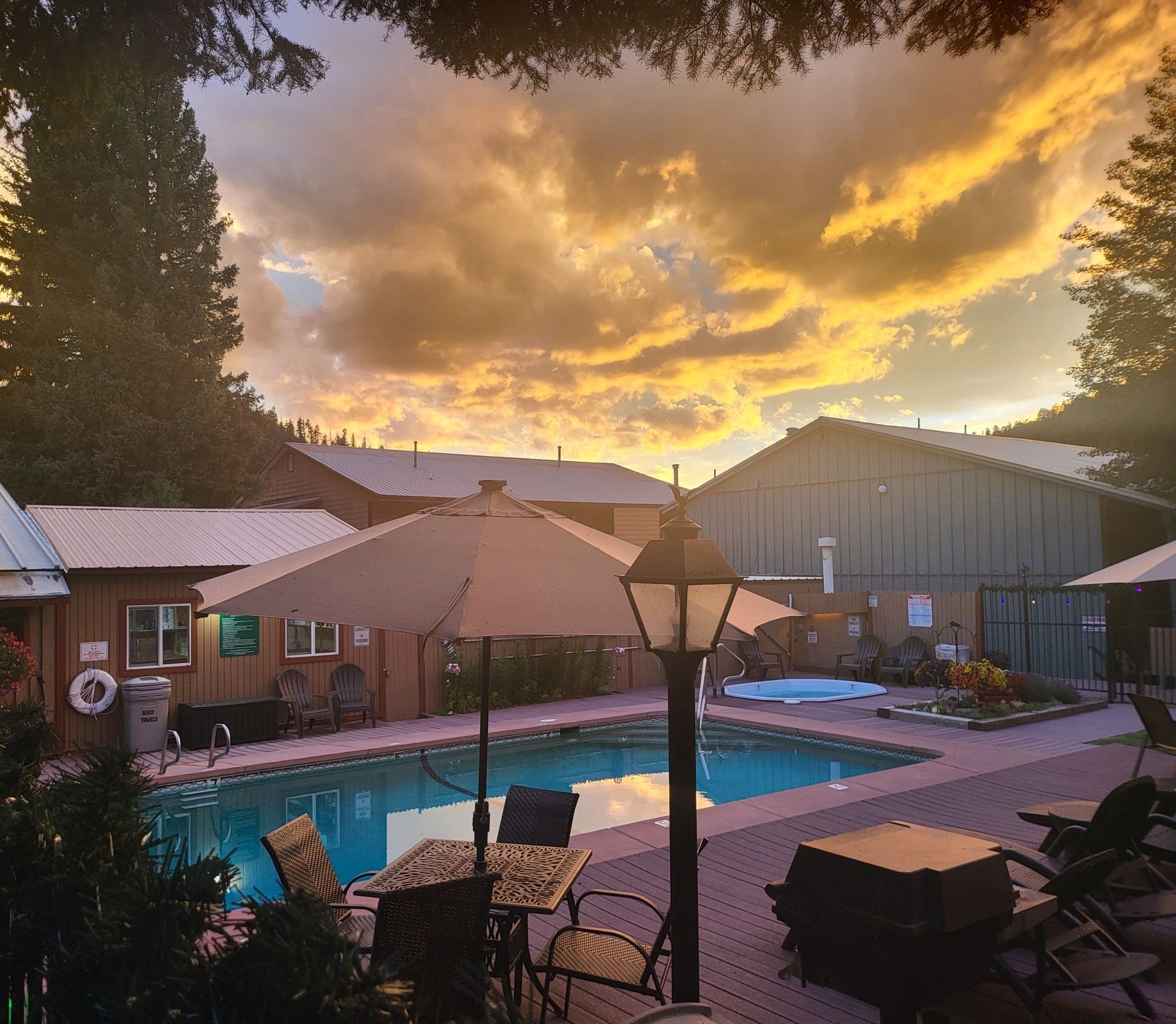 Sunset over a pool patio with umbrellas, lounge chairs, and a glowing cloudy sky