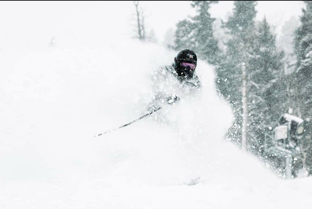 Skier in black jacket carving through deep powder on a snowy mountain slope