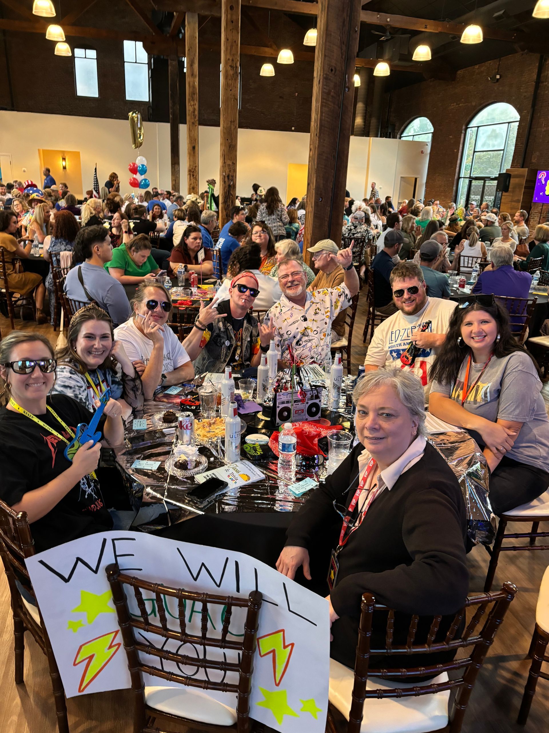 A group of people are sitting at a table with a sign that says `` we will ''.
