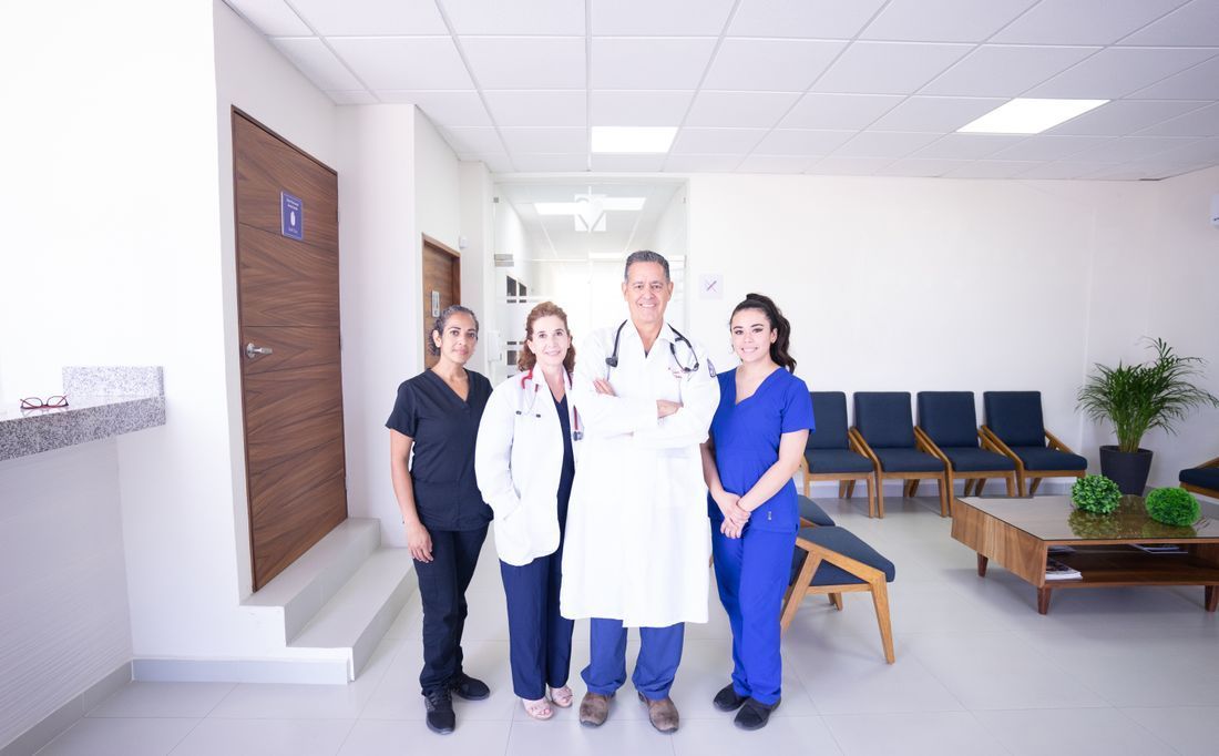 Four medical staff in scrubs and lab coats stand in a bright hospital waiting area.