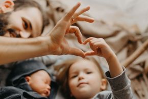 Hands forming a heart above two children resting on a bed