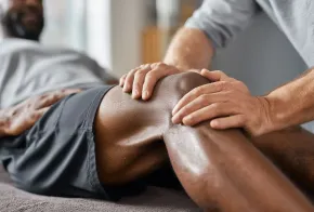 Hands massaging a person’s bent knee on a massage table, with a blurred person in the background