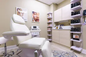 White treatment chair in a modern medical office with beige cabinets and skincare product shelves.