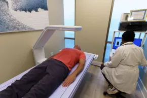 Person undergoing a medical scan while a technician operates the imaging machine nearby.
