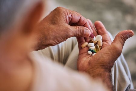 Hands holding assorted pills and capsules over a blurred background