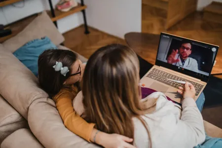 Two people on a couch watching a video call on a laptop in a cozy living room.