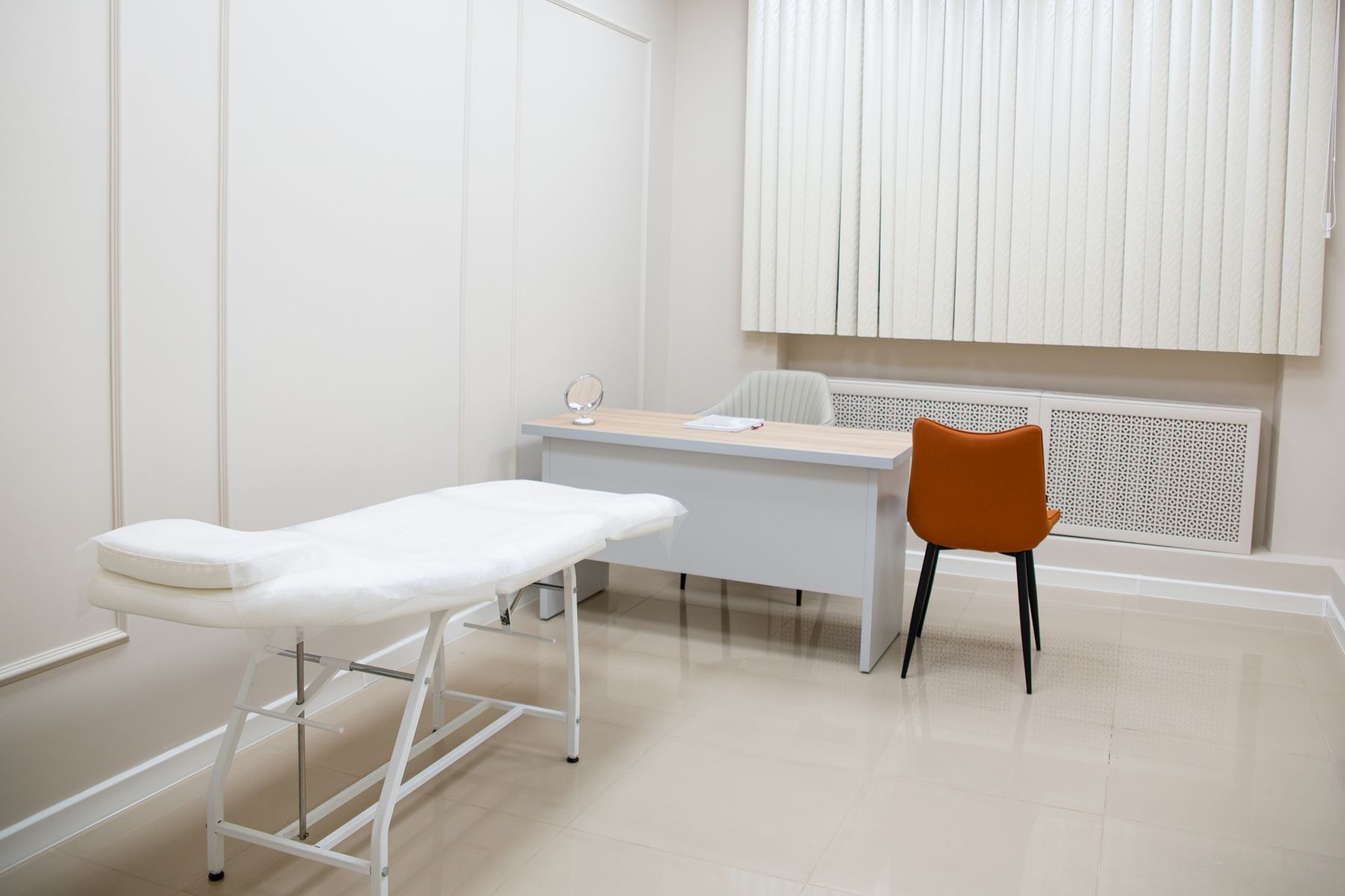 Minimal treatment room with a white examination table, desk, and orange chair