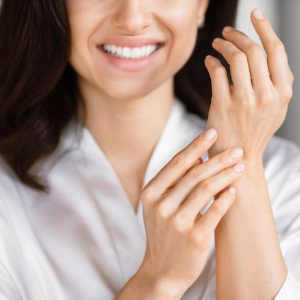 Smiling person in a white shirt rubbing their wrist with the other hand