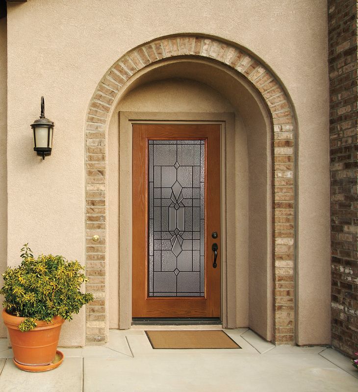 Front entrance with arched stone doorway, wooden glass door, potted plant, and wall lantern