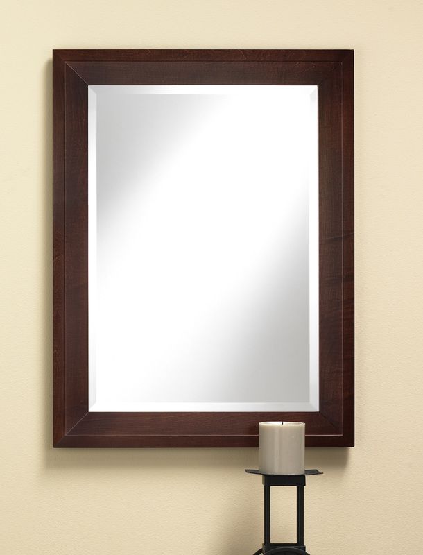 Wood-framed wall mirror above a small candle on a stand against a beige wall