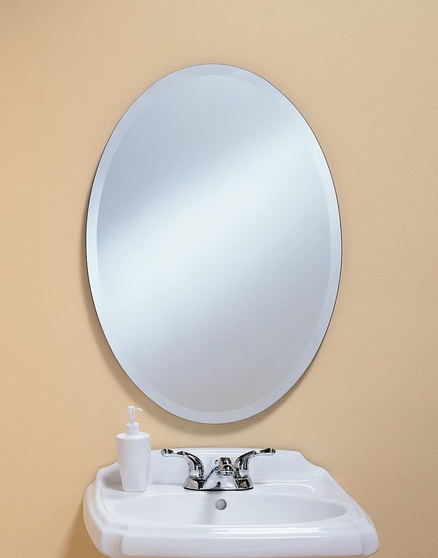 Oval mirror above a white bathroom sink with soap dispenser against a beige wall