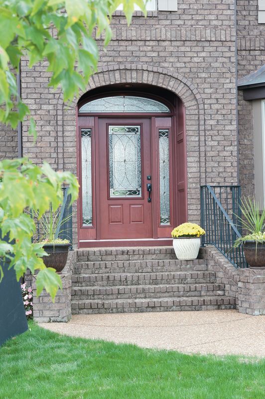 Front entrance of a brick house with red double doors, steps, and a potted yellow plant.