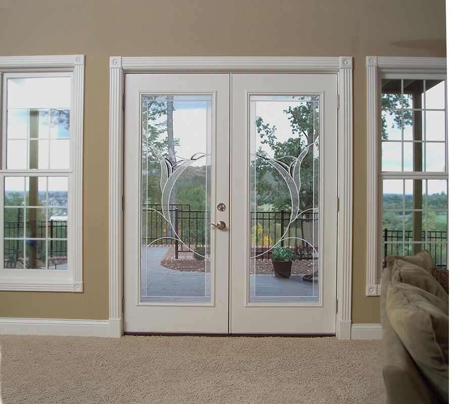 Bright living room with French doors opening to a patio and garden, flanked by windows and a beige sofa