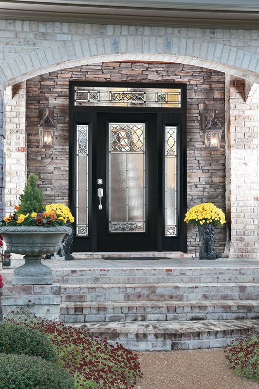Front entrance with black door, brick arch, and potted yellow flowers on stone steps