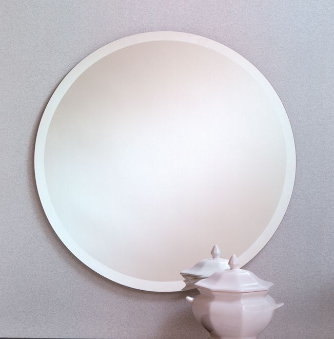 White round wall mirror above a small white vase with a flower on a light gray wall.