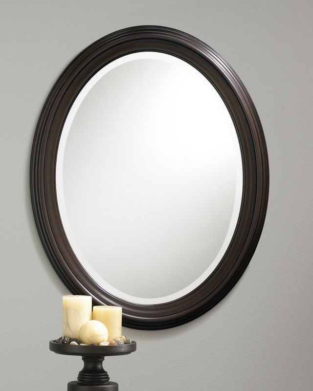 Oval black-framed mirror above a small table with two candles against a gray wall