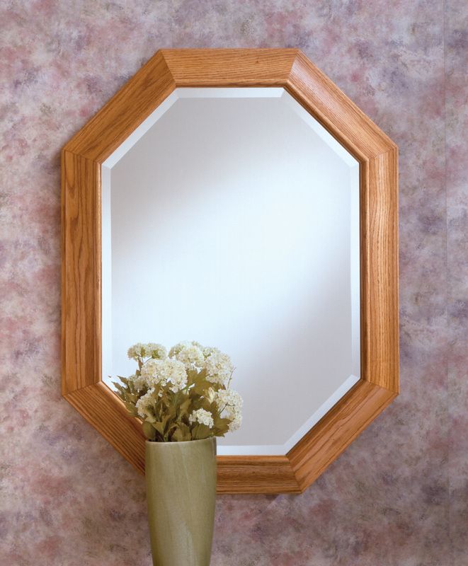 Octagonal wooden-framed mirror above a vase of white flowers on a mottled pink wall