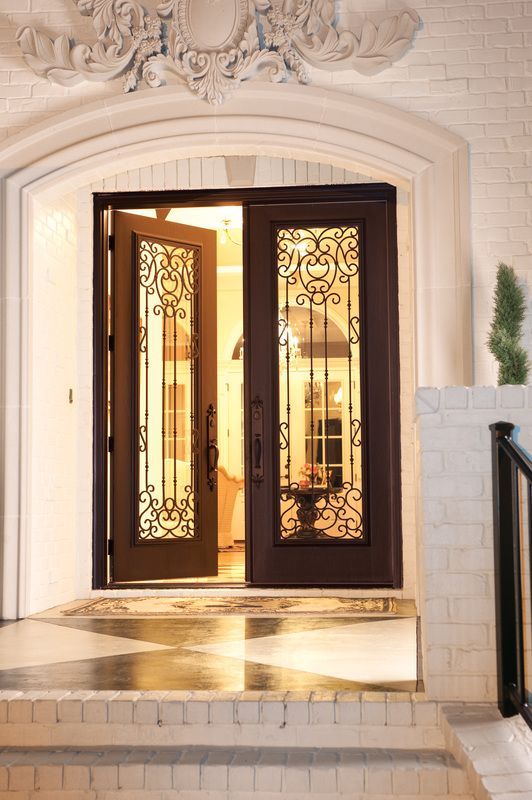 Open ornate double front doors with warm light glowing from inside a white stone entryway.