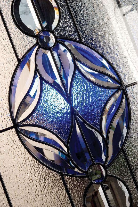 Blue and silver stained-glass pendant with leaf-like swirls on a textured wall