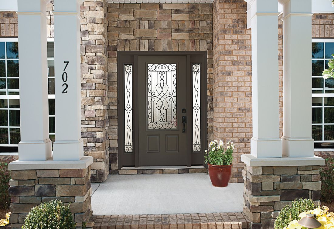 Front entrance of a brick house with white columns, dark door, and a potted plant by the steps.