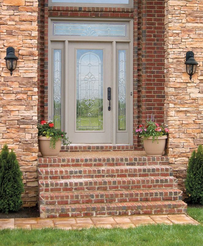 Brick house entry with double glass door, front steps, and potted flowers on either side