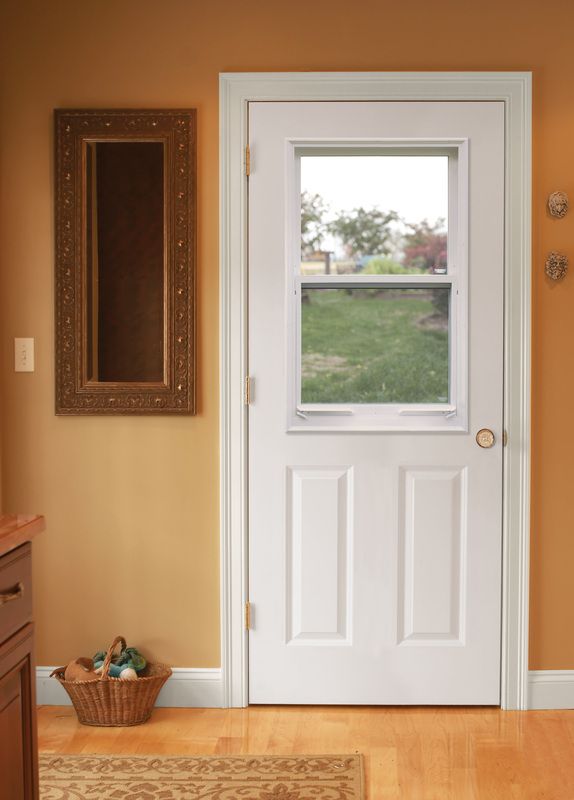 White front door with window, flanked by a mirror and hooks, in a warm-toned entryway.