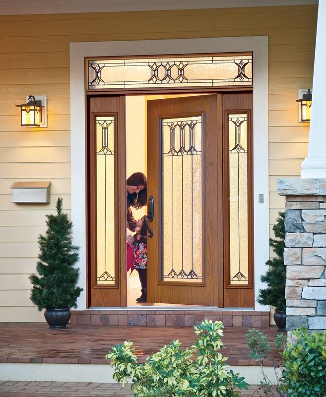 Person peeking through a front door at a house entrance, framed by sidelights and porch lights.