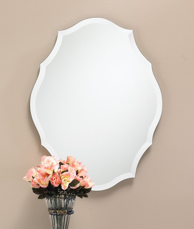 White ornate wall mirror above a black vase of pink flowers on a beige wall