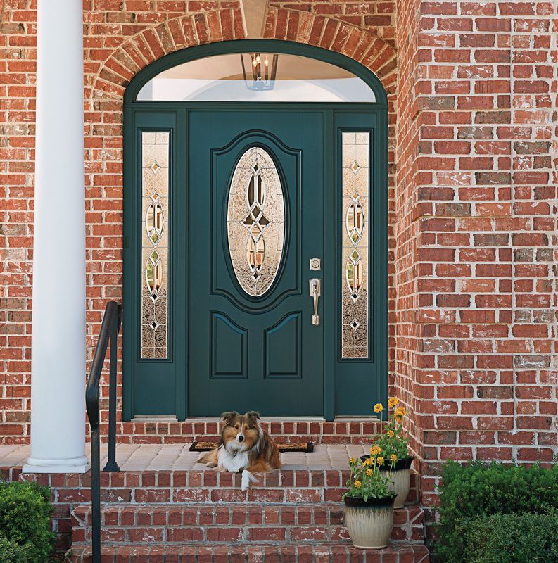 Dog lying on brick porch before a teal front door with arched glass and potted flowers