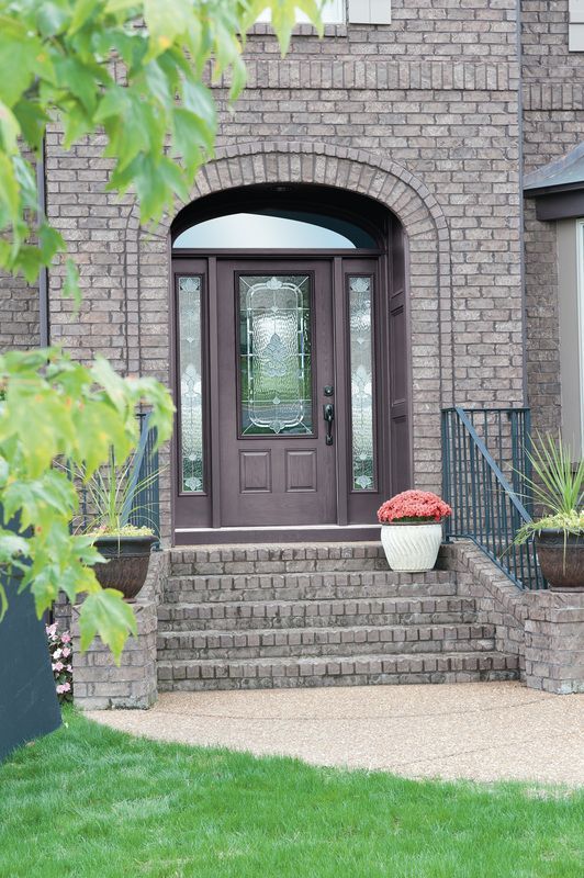 Brick house entry with arched doorway, dark front door, steps, and a potted flower on the porch
