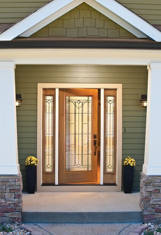Front porch with a wooden front door, glass sidelights, and two black planters with yellow flowers