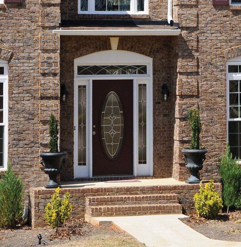 Brick house front entrance with brown door, small steps, and potted topiary plants