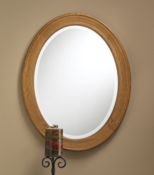 Oval wooden-framed wall mirror above a small candle holder on a beige wall