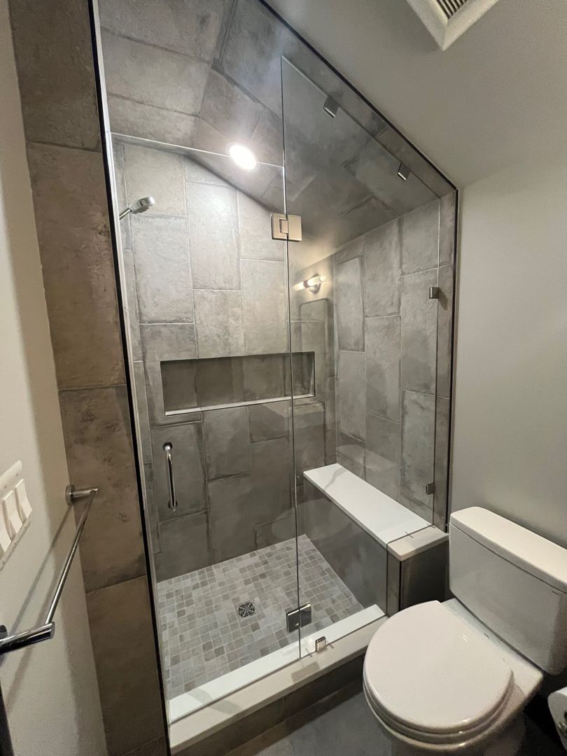 Small tiled accessible shower with built-in bench and adjacent toilet in a modern bathroom.