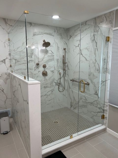 Modern glass-enclosed shower with marble-pattern walls, gold fixtures, and a tiled floor in a bathroom