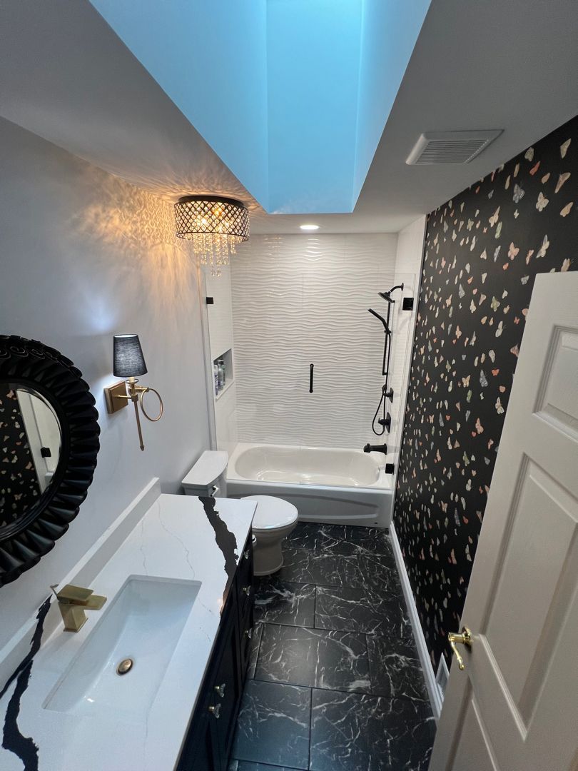 Modern bathroom with black tile, walk-in shower, blue-lit ceiling, and gold wall sconce