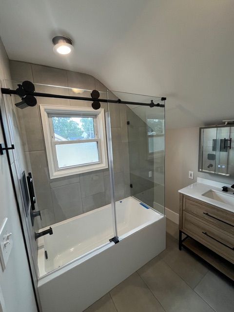 Modern bathroom with a walk-in tub, glass shower panel, window, and wood vanity