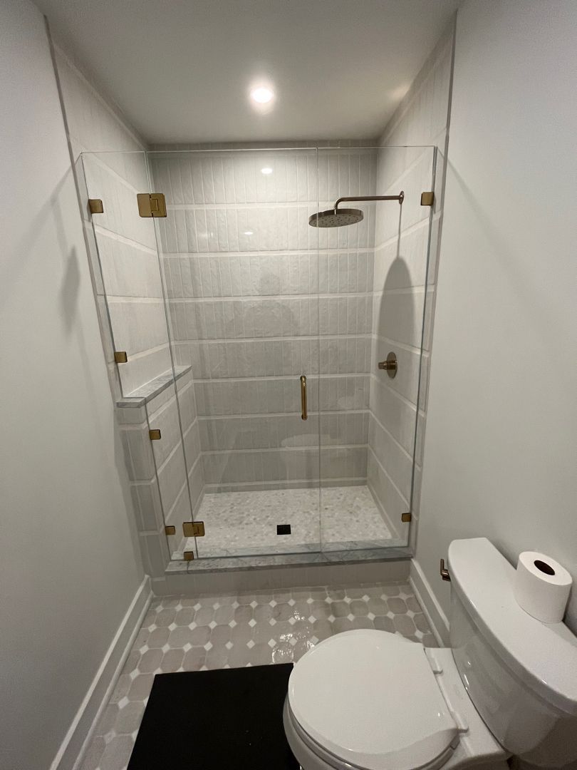 Small bathroom with walk-in shower, toilet, and gray tile walls, viewed from the doorway.
