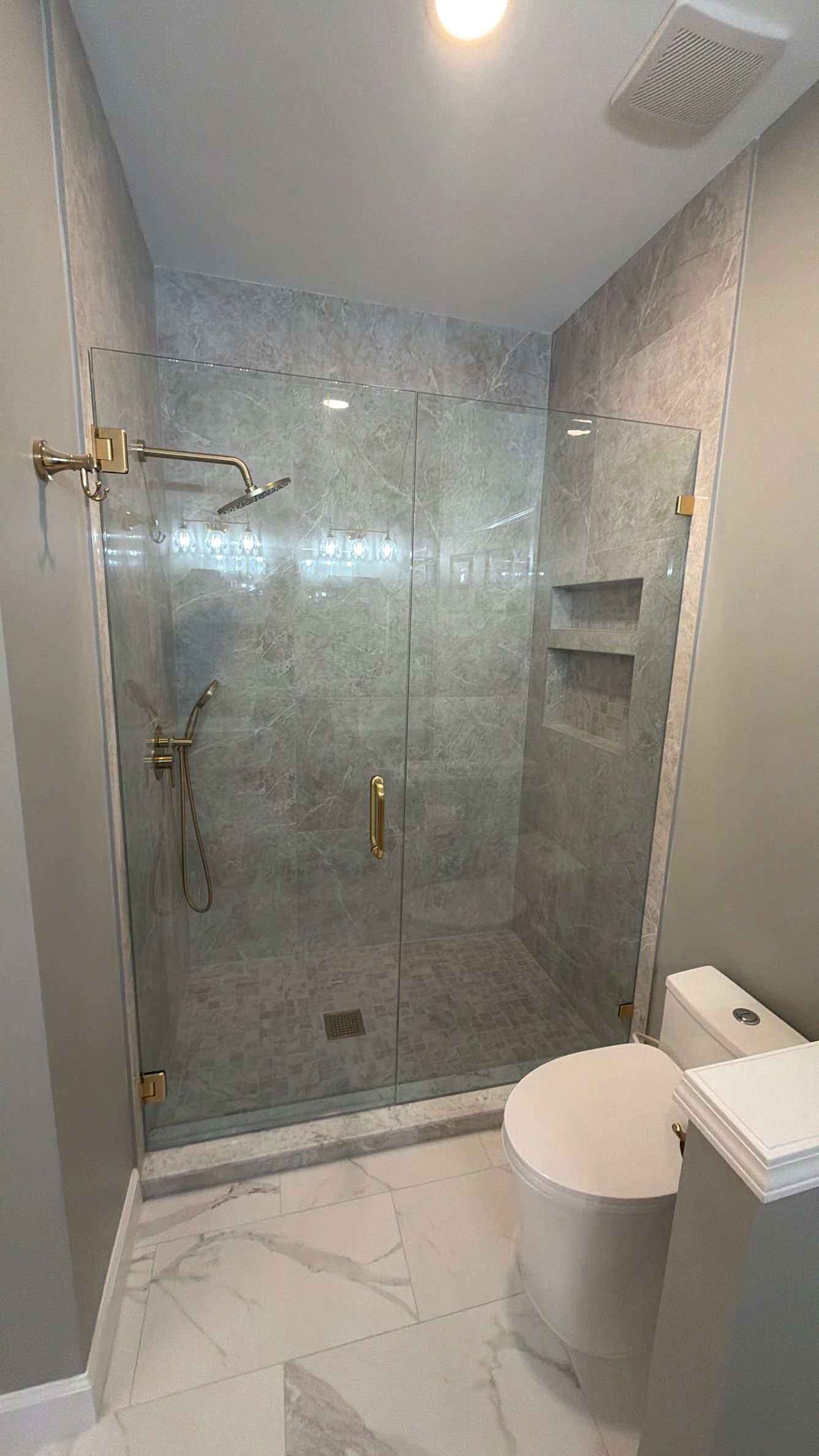 Modern bathroom with a glass walk-in shower, tiled walls, and a toilet in the foreground.