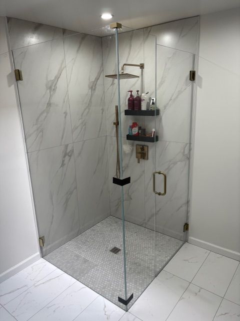 Modern shower with glass enclosure, marble-look tile walls, and built-in shelf in a bright bathroom
