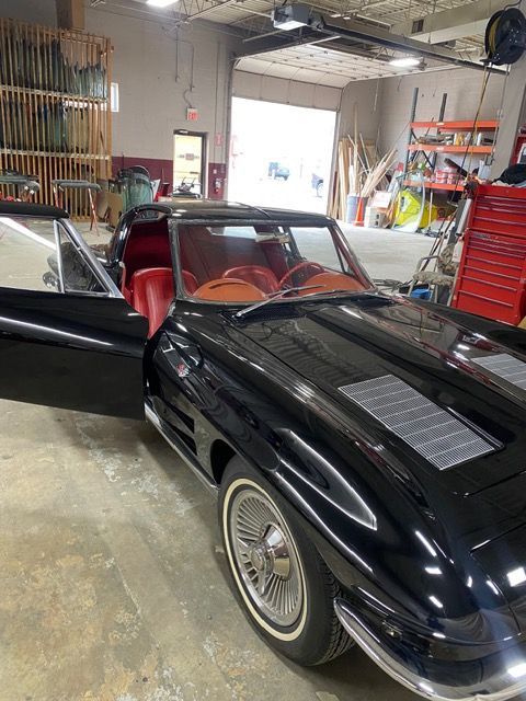 Black classic sports car with red interior in a garage, driver door open.