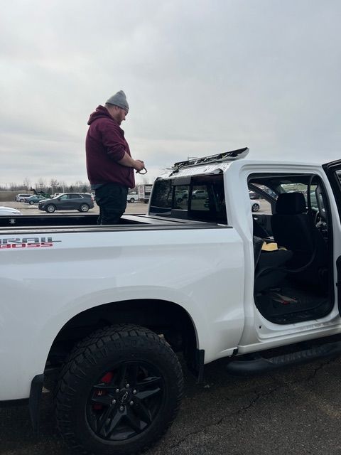 Person standing in a white pickup truck bed beside an open door in a cloudy parking lot
