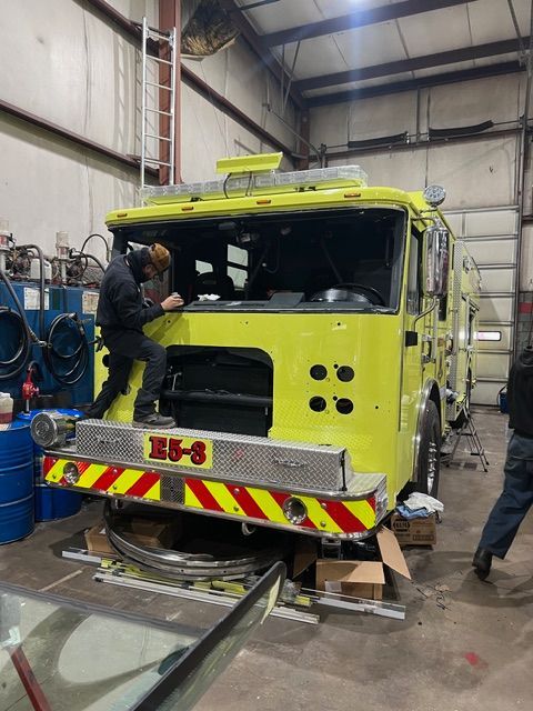 Yellow fire truck being repaired in a garage, with two workers around it.