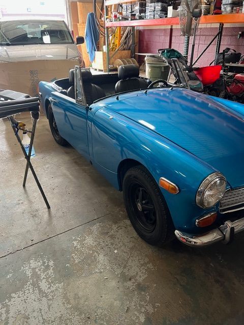 Blue classic convertible parked in a garage, with a beige car nearby and tools in the background