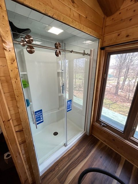 Glass shower enclosure in a wood-paneled bathroom with a window view outside.